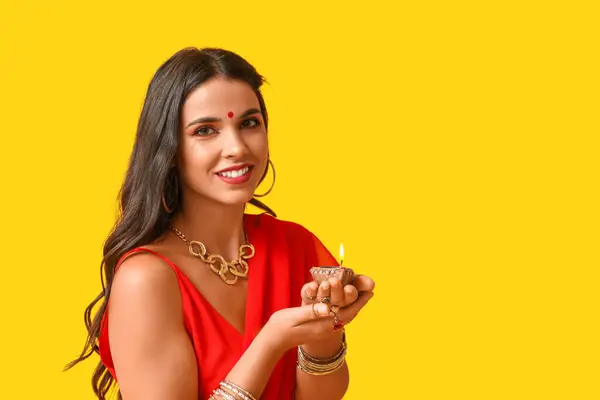 stock image Beautiful young happy Indian woman in traditional sari with burning candle on yellow background. Divaly celebration