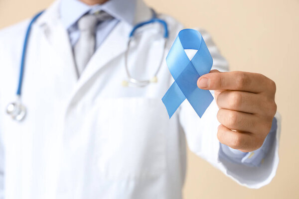 Male urologist with blue ribbon on beige background, closeup. Prostate cancer awareness concept