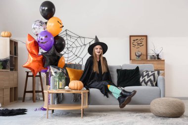 Cadılar Bayramı için giyinmiş, balonlu genç bir kadın evdeki kanepede oturuyor.