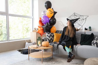 Cadılar Bayramı için giyinmiş, balonlu genç bir kadın evdeki kanepede oturuyor.