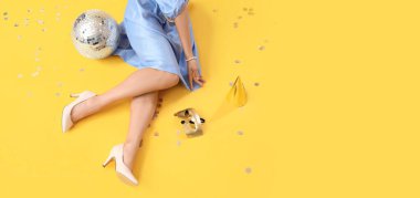 Sarı arka planda disko topu olan güzel genç bir kadının bacakları.