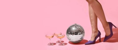 Yüksek topuklu ayakkabılı kadın bacakları, şampanya bardakları ve pembe arka planda disko topu ve mesaj için yer. Yeni yıl partisi konsepti