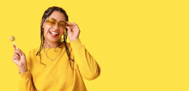 Sarı arka planda lolipopu olan havalı, Afro-Amerikalı genç bir kadın. Mesaj için yeri var.