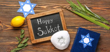 Four species (lulav, hadas, arava, etrog), paper David star, kippah and chalkboard with text HAPPY SUKKOT on wooden background clipart