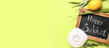 Dört tür (lulav, hadas, arava, etrog), kippah ve yazı tahtası ile yeşil arkaplanda metin için boşluk olan HAPPY SUKKOT