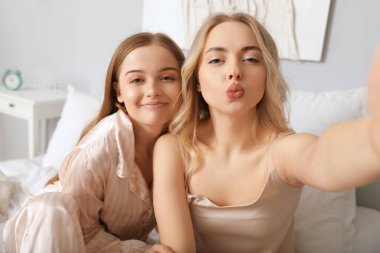 Genç kız kardeşler yatak odasında selfie çekiyorlar.