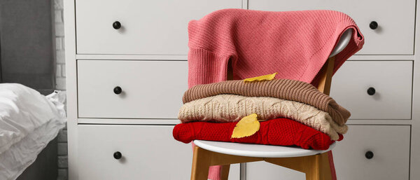 Warm sweaters with autumn leaves on chair in bedroom