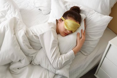 Genç bir kadının yatakta maskeyle uyuduğu bir sabah.