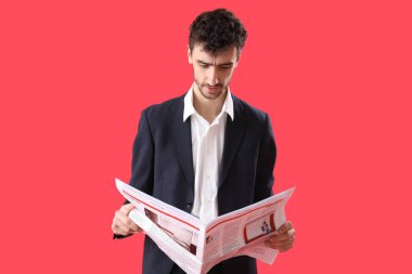 Takım elbiseli genç adam kırmızı arka planda gazete okuyor.