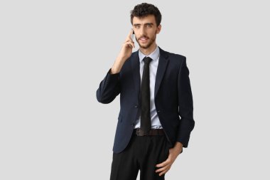 Takım elbiseli genç işadamı arka planda cep telefonuyla konuşuyor.