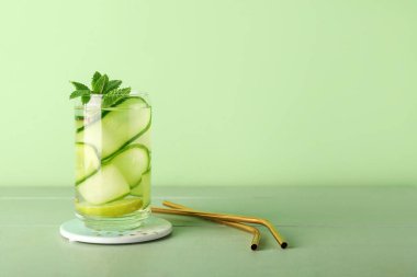 Yeşil ahşap masada salatalık dilimleri ile doldurulmuş bir bardak su.