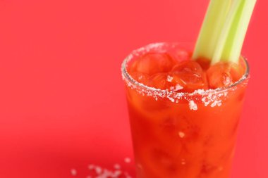 Kırmızı zemin üzerinde kereviz ve tuz olan bir bardak Bloody Mary.