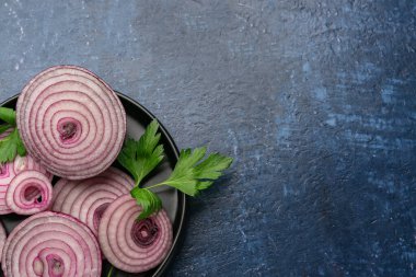 Taze soğan dilimleri ve mavi arka planda maydanoz yapraklı tabak.