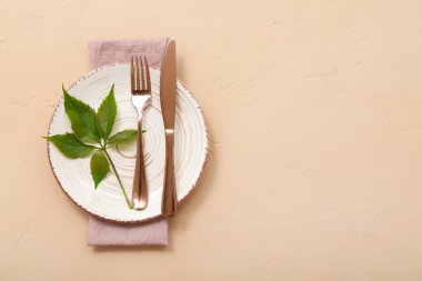 Temiz tabak, çatal bıçak ve yeşil bitki yapraklarıyla bej arka planda güzel bir masa.