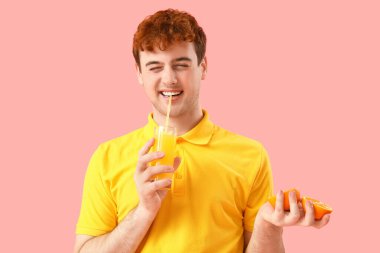 Pembe arka planda portakal suyu ve bir bardak meyve suyu olan genç bir adam.