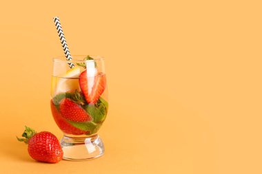 Turuncu arka planda çilekli ve limonlu bir bardak taze limonata.