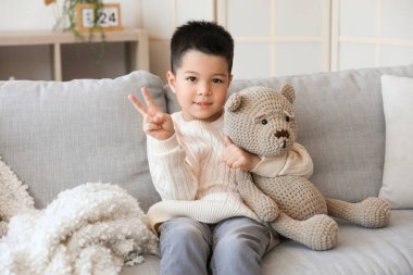 Evde zafer jesti yapan oyuncak ayıyla örülü süveter giyen sevimli küçük çocuk.