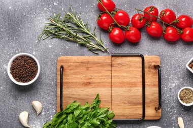 Ahşap mutfak tahtası, taze otlar, domatesler ve arkaplanda baharatlar.