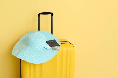 Hasır şapkalı bavul, pasaport, bilet ve sarı arka planda para. Seyahat kavramı