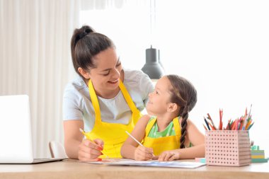 Küçük kız ve çalışan annesi mutfakta resim çiziyor.