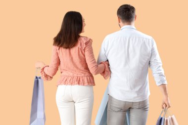 Bej arka planda alışveriş torbaları olan mutlu genç bir çift.