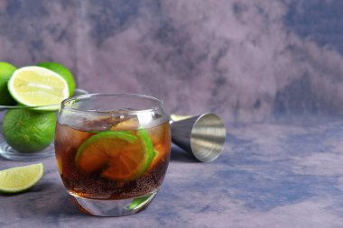 Bir bardak soğuk Küba Libre kokteyli ve mor arka planda limonlu kase.