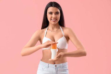 Pembe arka planda güneş kremi sürmüş genç bir kadın.