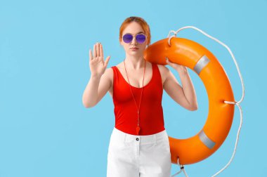 Yüzük şamandıralı kadın cankurtaran mavi arka planda dur işareti gösteriyor.