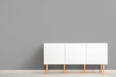 Gri duvarın yanındaki beyaz çekmeceler.