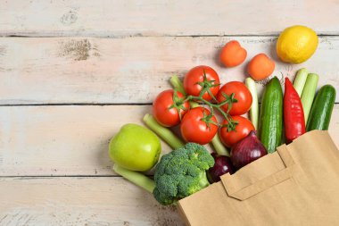 Taze sebzeli kağıt torba ve hafif ahşap arka planda meyveler.