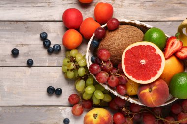 Gri ahşap arka planda farklı taze meyveler olan hasır kase.