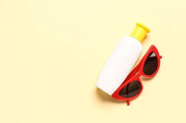 Soluk sarı arka planda güneş kremi şişeli güneş gözlüğü.