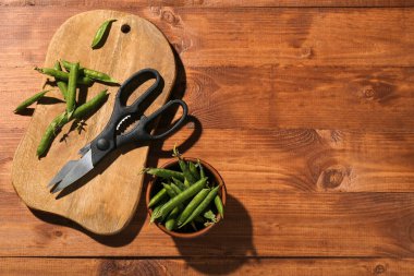 Yeni kesme tahtası, makas ve ahşap zemin üzerinde yeşil bezelye kabı