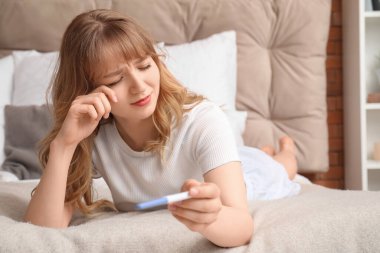 Yatak odasında hamilelik testi olan üzgün genç bir kadın.