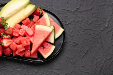 Taze karpuz parçalarıyla dolu tepsi ve siyah arkaplanda farklı böğürtlen