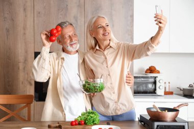 Domatesli olgun bir çift mutfakta selfie çekiyor.