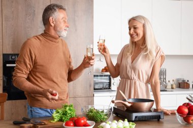 Olgun bir çift mutfakta şampanya içiyor.