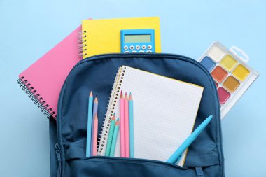 Mavi arkaplanda boş defter ve kırtasiye malzemesi olan sırt çantası
