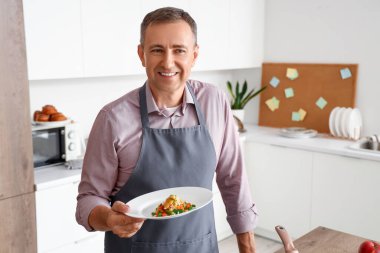 Mutfakta kızarmış sebzeli olgun bir adam.