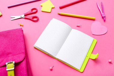 Boş defterli sırt çantası ve pembe arka planda farklı kırtasiye malzemesi.