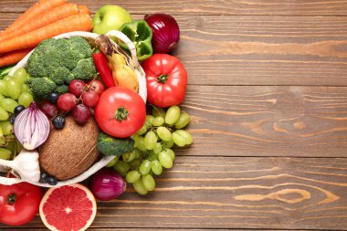 Tahta arka planda farklı taze meyve ve sebzelerle dolu sepet.