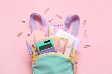 Hesap makinesi, not defteri ve pembe arkaplanda işaretler olan renkli okul çantası
