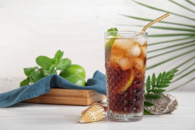 Bir bardak soğuk Küba kokteyli, taş ve deniz kabukları beyaz ahşap masada.