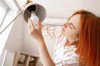 Evdeki masa lambasında ampulü değiştiren genç ve güzel bir kadın.