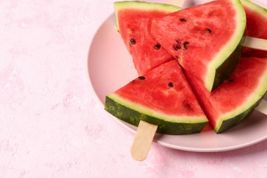Pembe arka planda tatlı karpuz çubukları olan bir tabak.