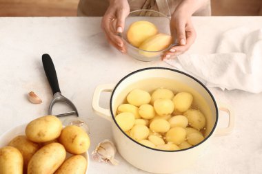 Elinde patates kabuğu ve soyulmuş sebzeli çömlek olan bir kadın.