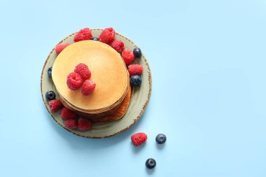 Mavi arka planda ahududu ve yaban mersinli bir tabak lezzetli krep.