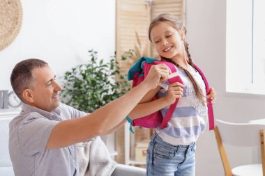 Babası küçük kızına okul çantasını takması için yardım ediyor.