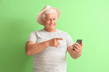 Yeşil arka planda cep telefonuna bakan kıdemli bir adam.