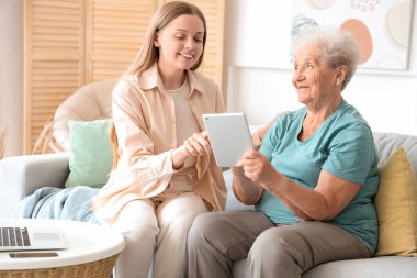 Torunuyla birlikte evde tablet bilgisayar kullanan yaşlı bir kadın.